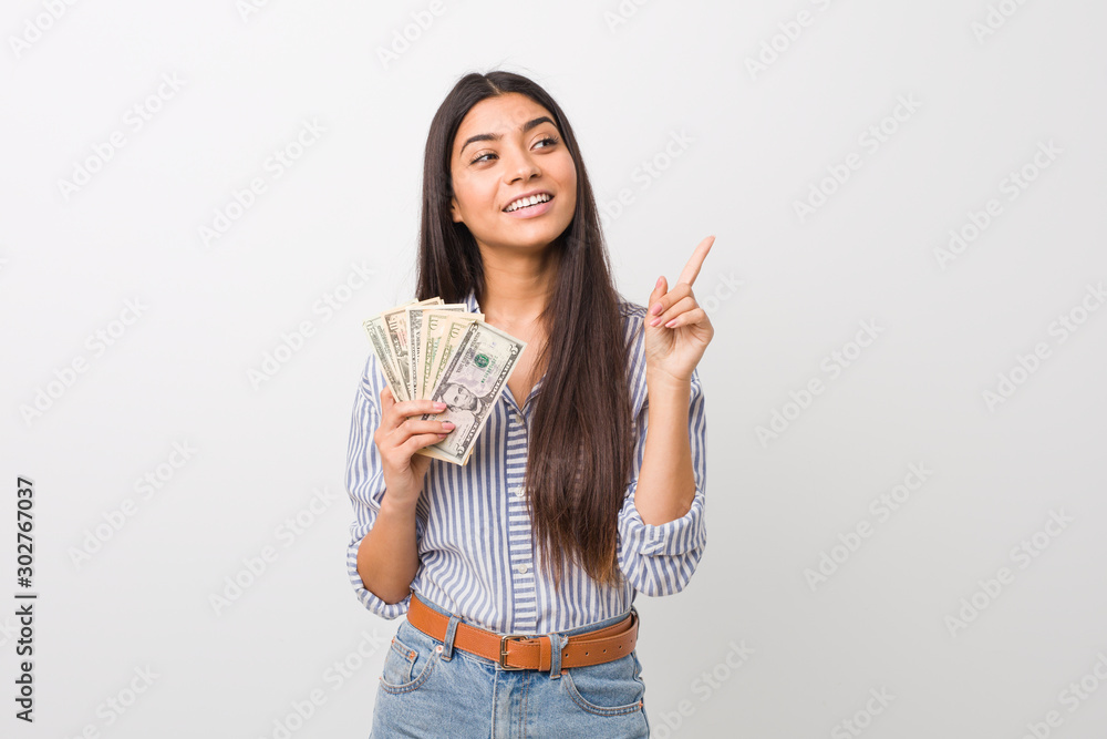 Young arab woman holding dollars smiling cheerfully pointing with forefinger away. Young arab woman holding dollars smiling cheerfully pointing with forefinger away.