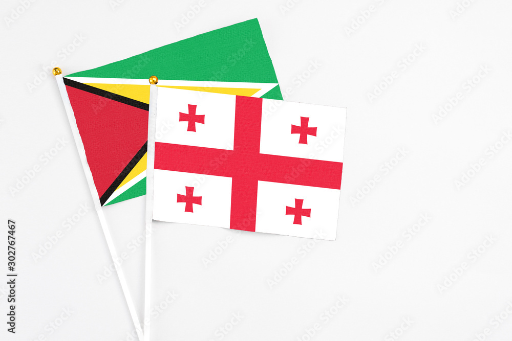 Georgia and Guyana stick flags on white background. High quality fabric, miniature national flag. Peaceful global concept.White floor for copy space.