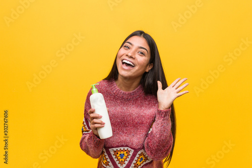 Young arab woman holding a cream bottle celebrating a victory or success