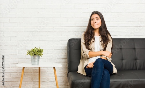 Young arab woman sitting on the sofa confused, feels doubtful and unsure.