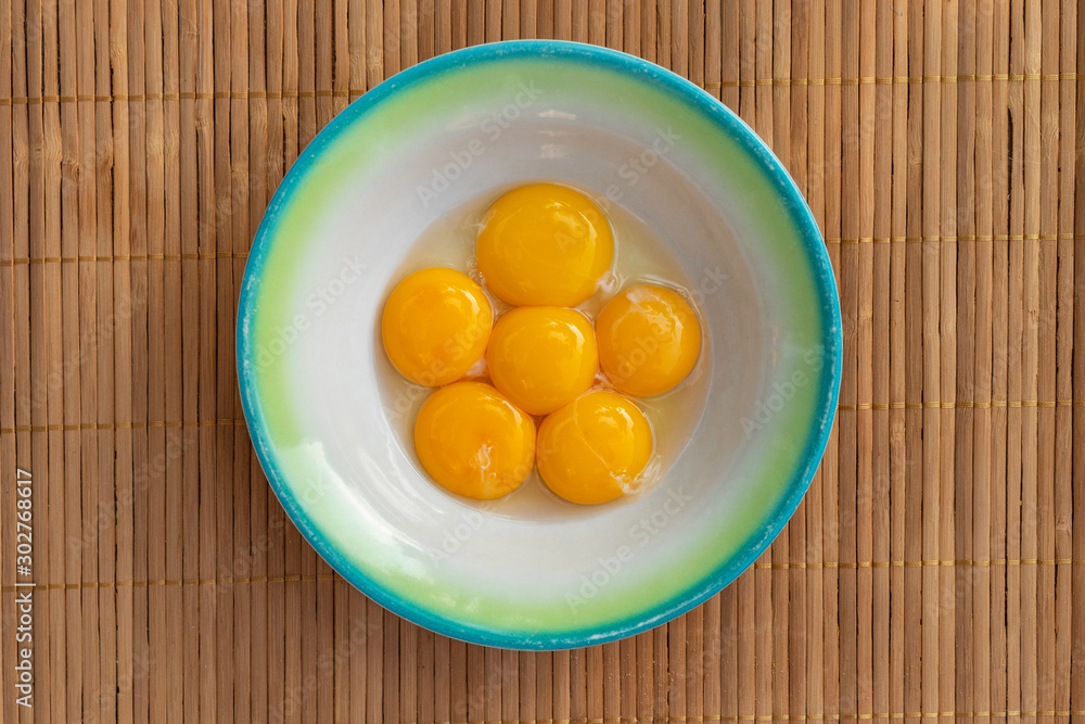 Chicken yolks lie in a white plate with a green border on a brown wooden litter Chicken yolks lie in a white plate with a green border on a brown wooden litter