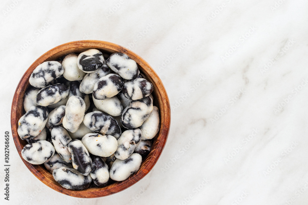 Black beans covered with salt lie in a brown bowl on a white marble surface Black beans covered with salt lie in a brown bowl on a white marble surface