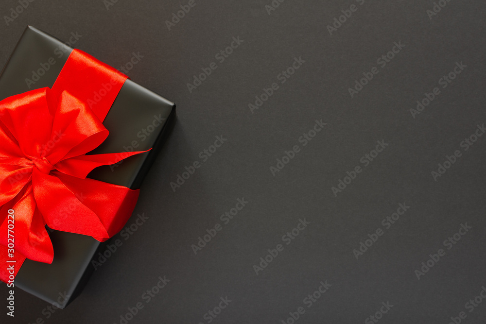 Festive background with gift, black gift box with red ribbon and bow on black background, black friday concept, flat lay, top view - obrazy, fototapety, plakaty 