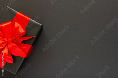 Festive background with gift, black gift box with red ribbon and bow on black background, black friday concept, flat lay, top view