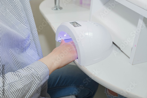 Woman is drying her nails in a UV lamp in a nail salon.