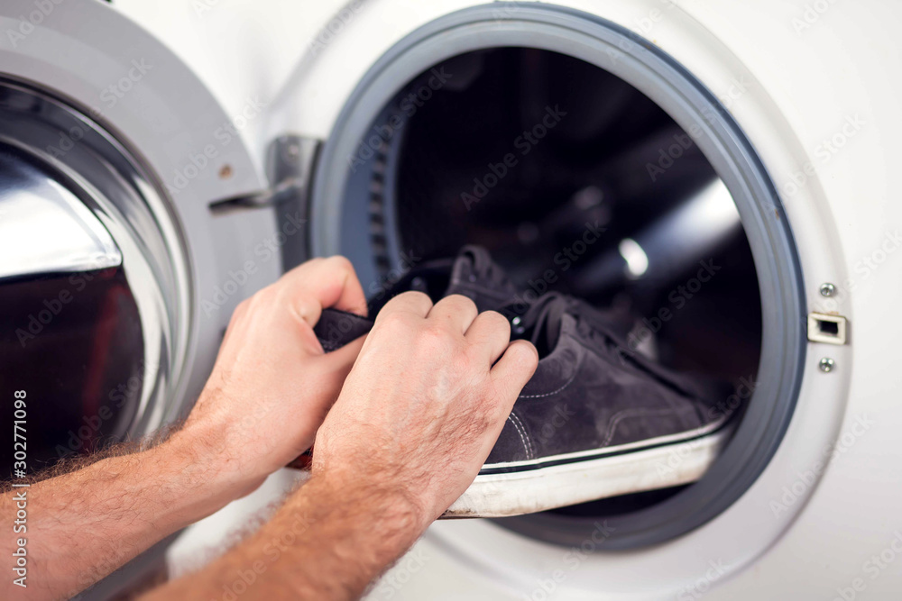 Loading sheakers in washing machine. Housework and laundry concept Loading sheakers in washing machine. Housework and laundry concept