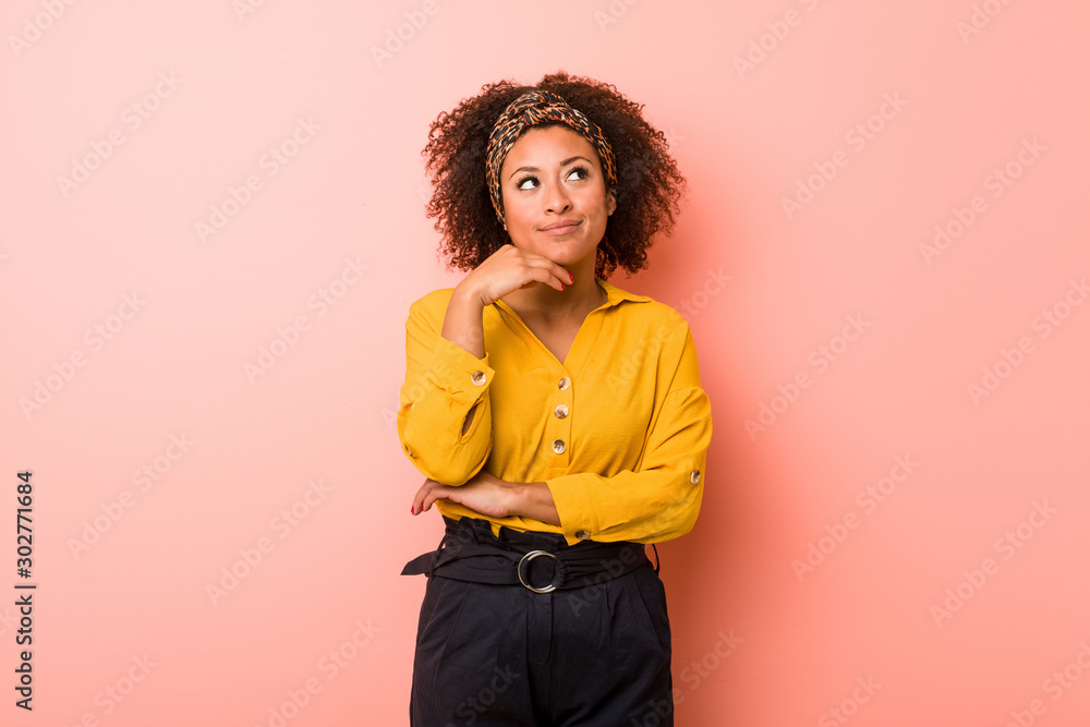 Young african american woman against a pink background looking sideways with doubtful and skeptical expression. Young african american woman against a pink background looking sideways with doubtful and skeptical expression.