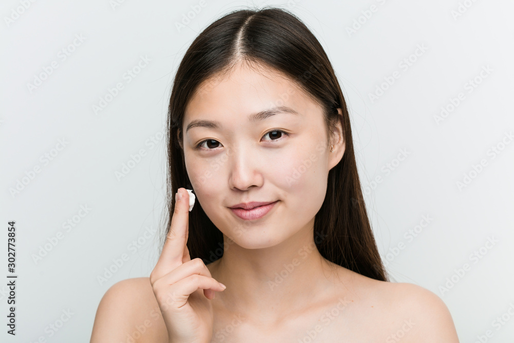 Close up of a young beautiful and natural asian woman applying a moisturizing cream Close up of a young beautiful and natural asian woman applying a moisturizing cream