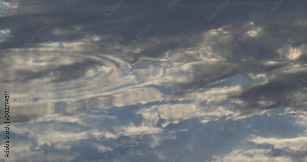 Close up of clouds reflection over calm water surface. Distorsion of sky image by the ripple movements of the river. Nature textures. Close up of clouds reflection over calm water surface. Distorsion of sky image by the ripple movements of the river. Nature textures.