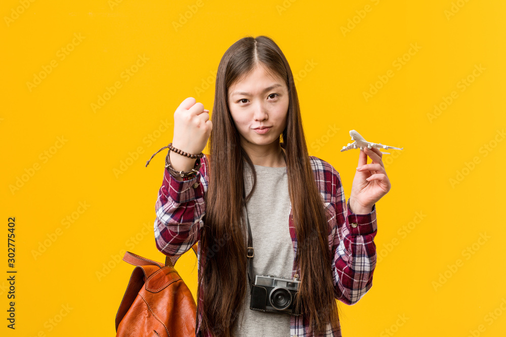 Young asian woman holding a airplane icon showing fist to camera, aggressive facial expression. Young asian woman holding a airplane icon showing fist to camera, aggressive facial expression.