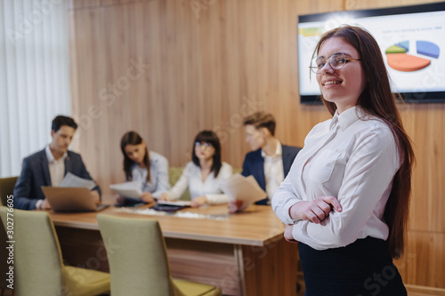 young attractive stylish office worker girl in glasses with a notebook in the hands on background of working colleagues