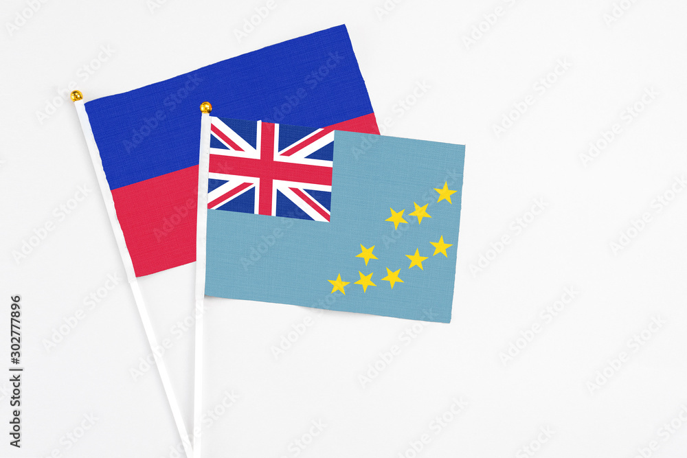 Fototapeta premium Tuvalu and Haiti stick flags on white background. High quality fabric, miniature national flag. Peaceful global concept.White floor for copy space.