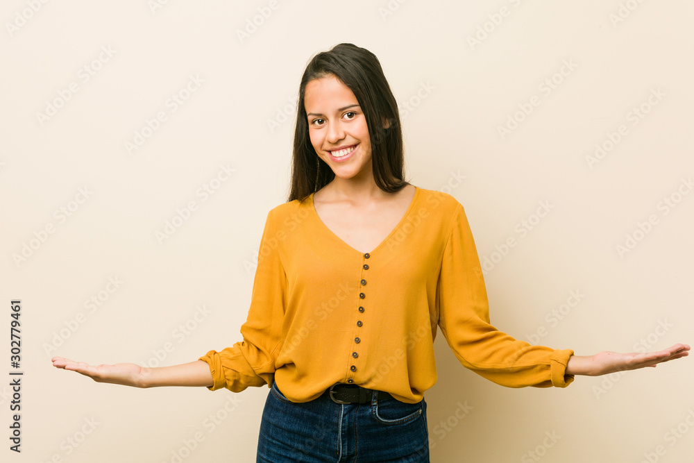Young hispanic woman against a beige background showing a welcome expression. Young hispanic woman against a beige background showing a welcome expression.