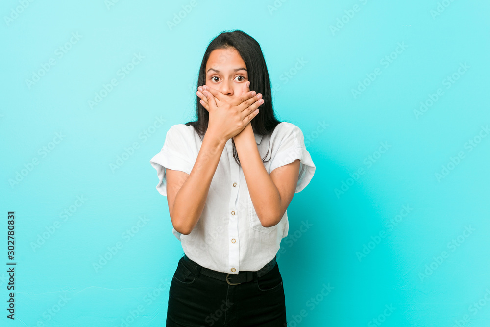 Young hispanic cool woman against a blue wall shocked covering mouth with hands.