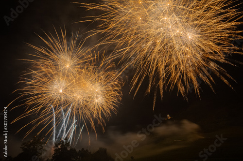 Multi explosions of golden fireworks over trees silhouette and over an illuminated church  Vittorio Veneto  Italy