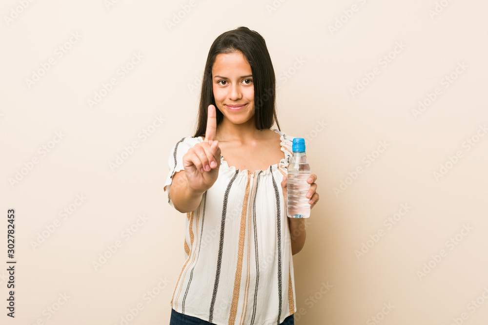 Young hispanic woman holding a bottle of water showing number one with finger. Young hispanic woman holding a bottle of water showing number one with finger.