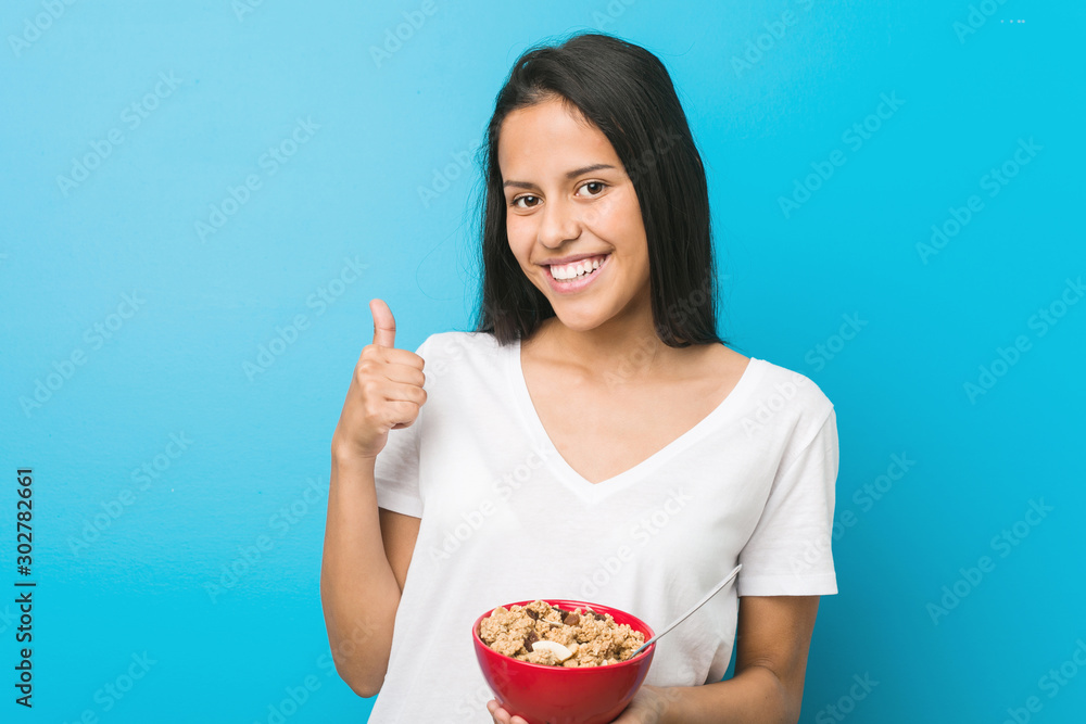 Young hispanic woman holding a cereal bowl smiling and raising thumb up Young hispanic woman holding a cereal bowl smiling and raising thumb up