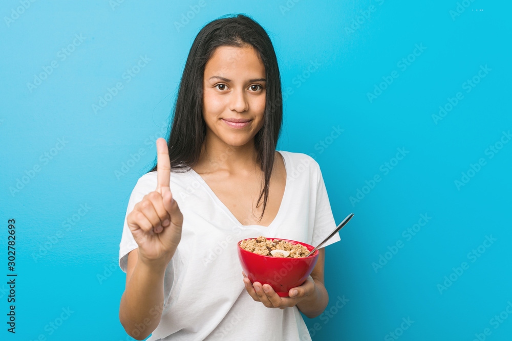 Young hispanic woman holding a cereal bowl showing number one with finger. Young hispanic woman holding a cereal bowl showing number one with finger.
