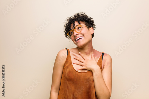 Young african american woman with skin birth mark laughs out loudly keeping hand on chest.