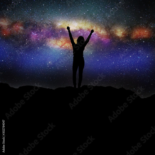 Frau steht nachts auf einem Berg vor einem Sternenhimmel