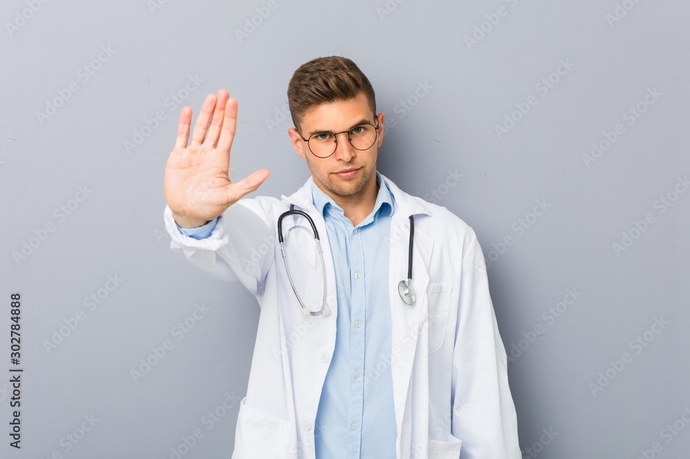 Young blonde doctor man standing with outstretched hand showing stop sign, preventing you. Young blonde doctor man standing with outstretched hand showing stop sign, preventing you.