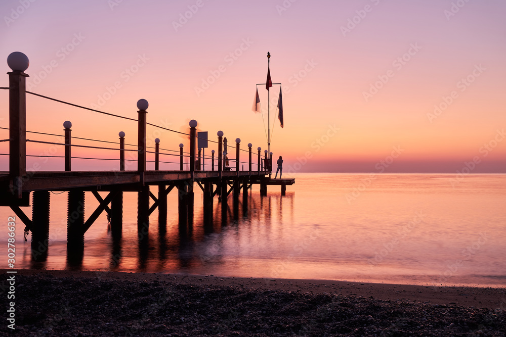 Silhouette of a girl standing on a large wooden pier against the backdrop of a stunning sunrise at sea