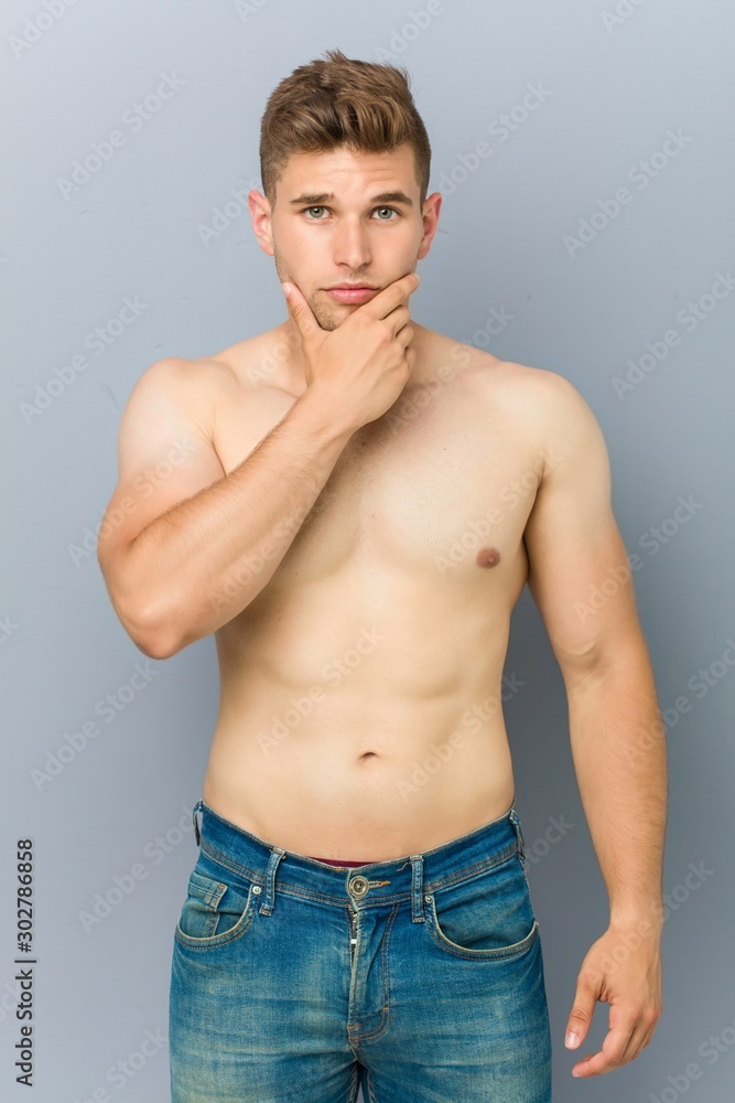 Young caucasian fitness man shirtless touching his chin.