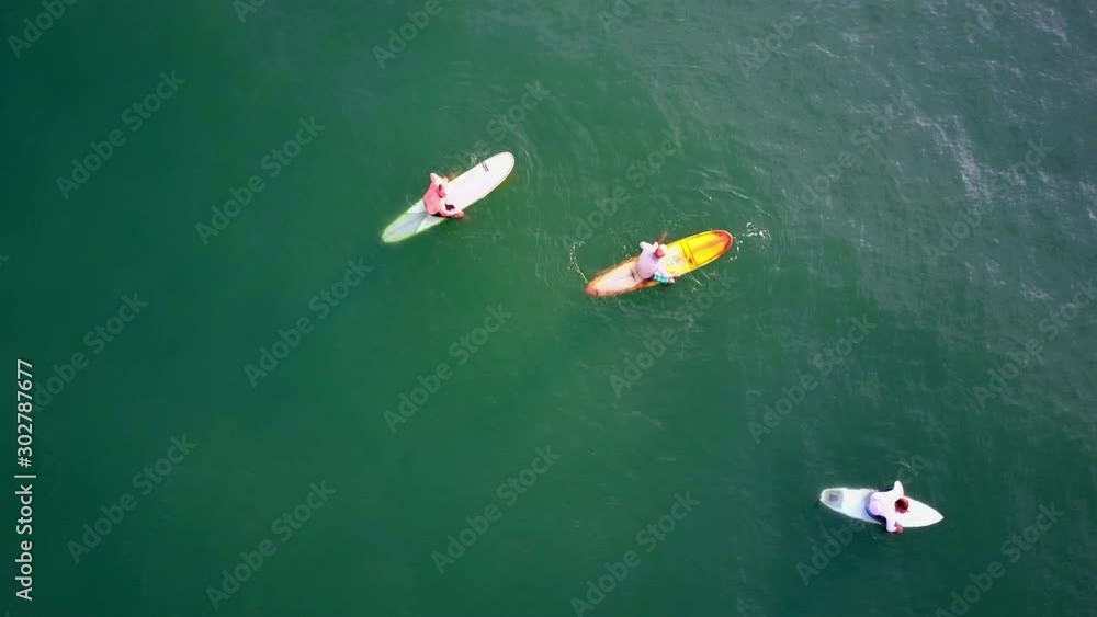 Three male surfers sitting on floating surfboards in ocean, aerial straight above Three male surfers sitting on floating surfboards in ocean, aerial straight above