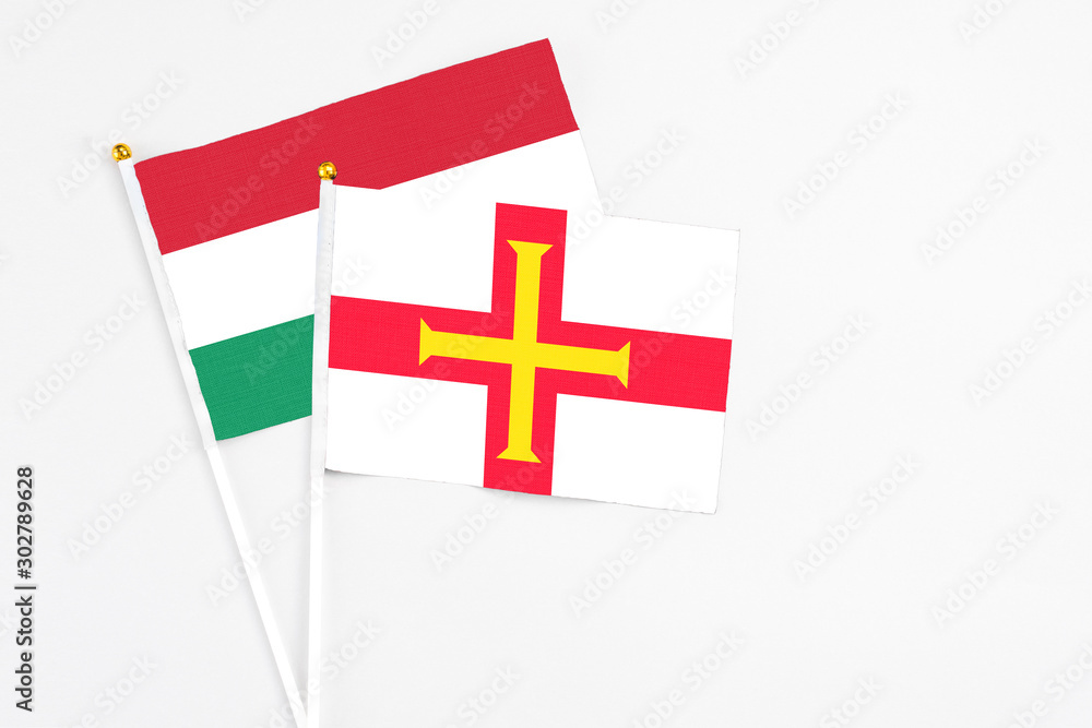 Guernsey and Hungary stick flags on white background. High quality fabric, miniature national flag. Peaceful global concept.White floor for copy space.