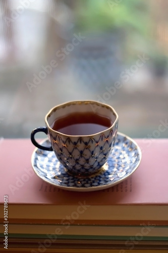 Tea in a vintage porcelain cup on stack of pastel colored books. Selective focus.