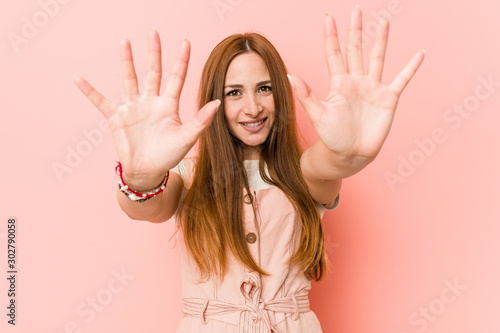 Young ginger woman with freckles showing number ten with hands.