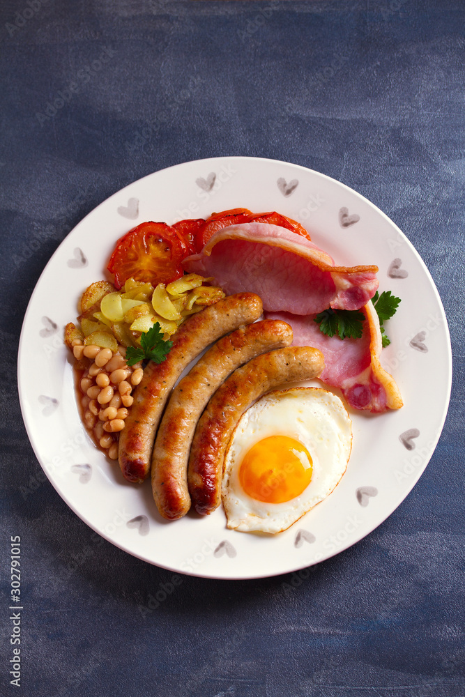 Sausages, bacon, egg, tomatoes, fries and beans on white plate. Overhead vertical image Sausages, bacon, egg, tomatoes, fries and beans on white plate. Overhead vertical image