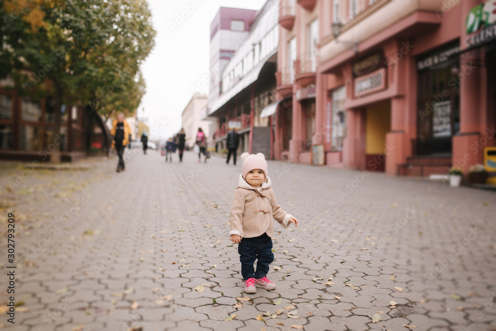 Adorable little baby girl in beautiful brown coat walking in the city. Cute eleven month baby smile and run