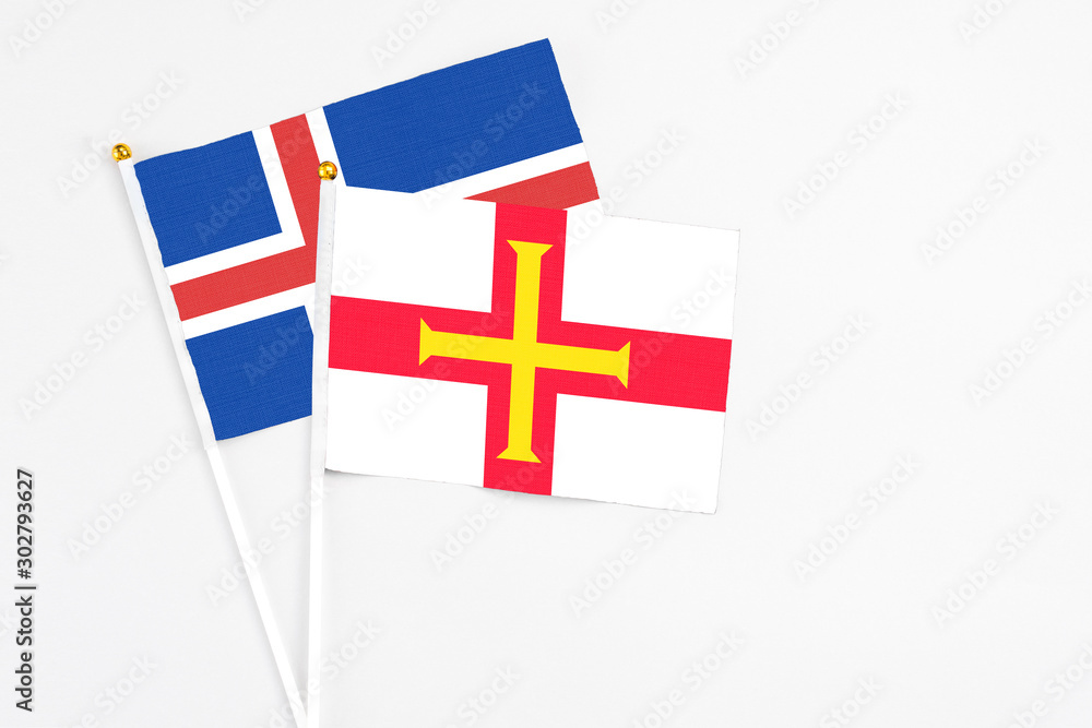 Guernsey and Iceland stick flags on white background. High quality fabric, miniature national flag. Peaceful global concept.White floor for copy space.