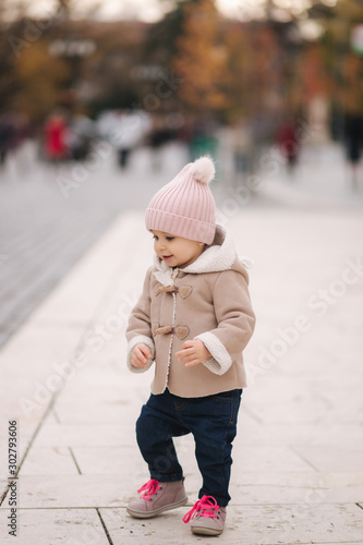 Cute eleven month baby girl dance in the centre of the city. Happy little girl outside in autumn