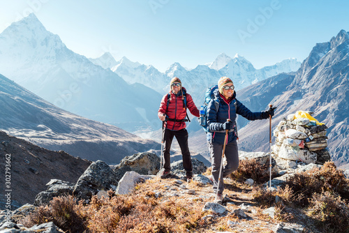 Couple following Everest Base Camp trekking route near Dughla 4620m. Backpackers carrying Backpacks and using trekking poles and enjoying valley view with Ama Dablam 6812m peak photo