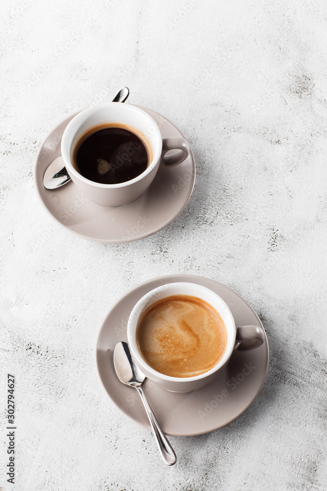 Two white cups of hot black coffee with milk isolated on bright marble background. Overhead view, copy space. Advertising for cafe menu. Coffee shop menu. Vertical photo.