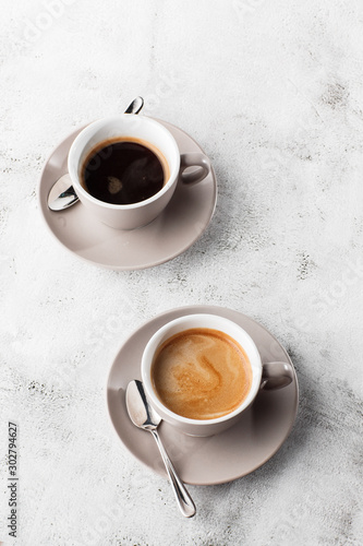 Obraz na płótnie Two white cups of hot black coffee with milk isolated on bright marble background. Overhead view, copy space. Advertising for cafe menu. Coffee shop menu. Vertical photo. w salonie