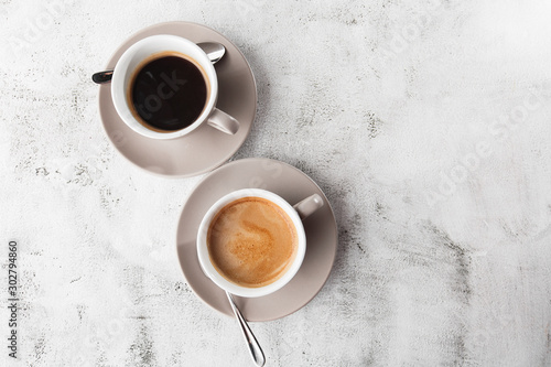 Two white cups of hot black coffee with milk isolated on bright marble background. Overhead view, copy space. Advertising for cafe menu. Coffee shop menu. Horizontal photo.