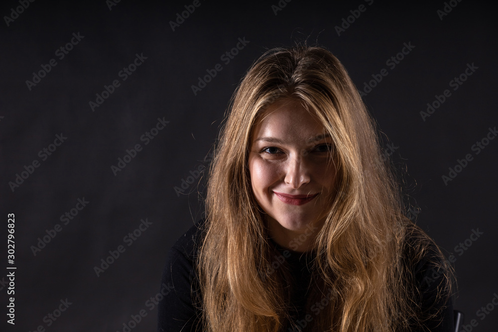 young beautiful blonde girl with a slight smirk on her face on a dark background young beautiful blonde girl with a slight smirk on her face on a dark background