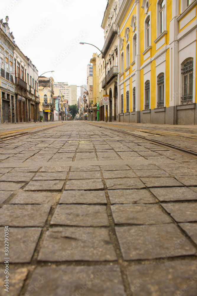 Details of paving stones of an ancient street at the historic center of Rio de Janeiro with yellow historic building and VLT trails
