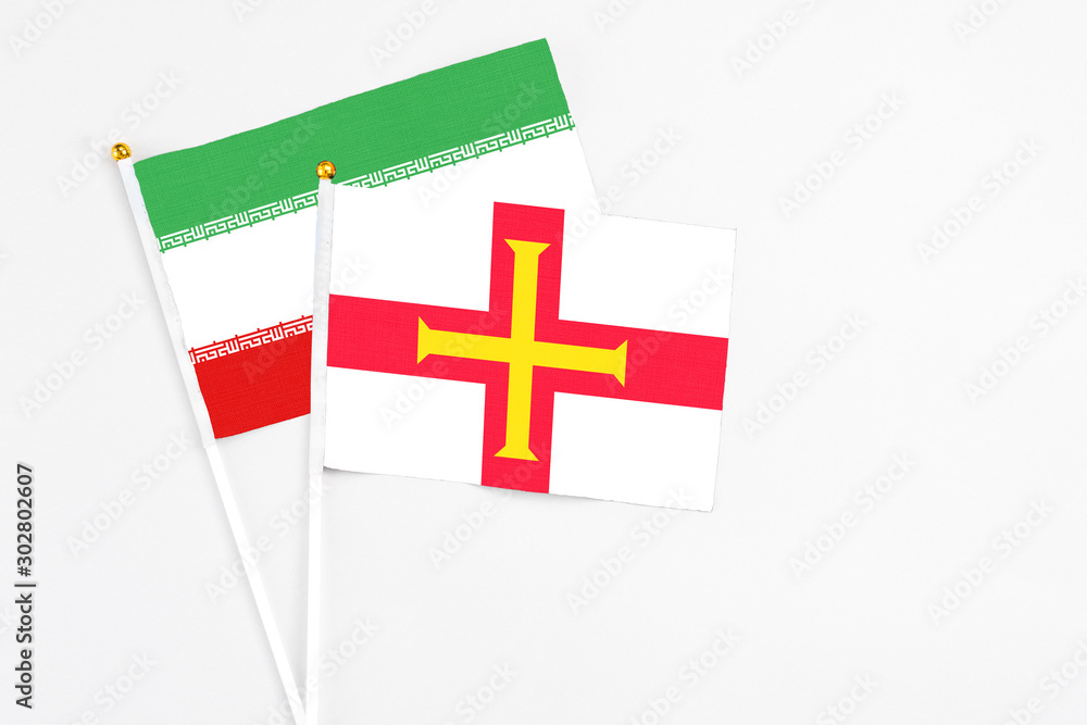 Guernsey and Iran stick flags on white background. High quality fabric, miniature national flag. Peaceful global concept.White floor for copy space.