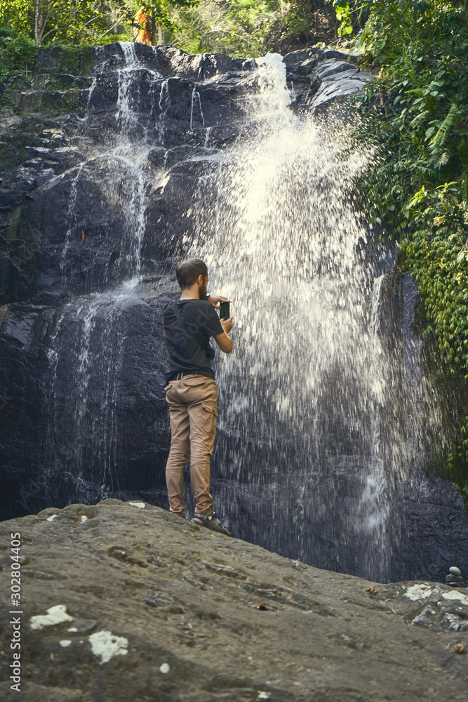 Human standing on the big stone opposite wild nature waterfall view Human standing on the big stone opposite wild nature waterfall view