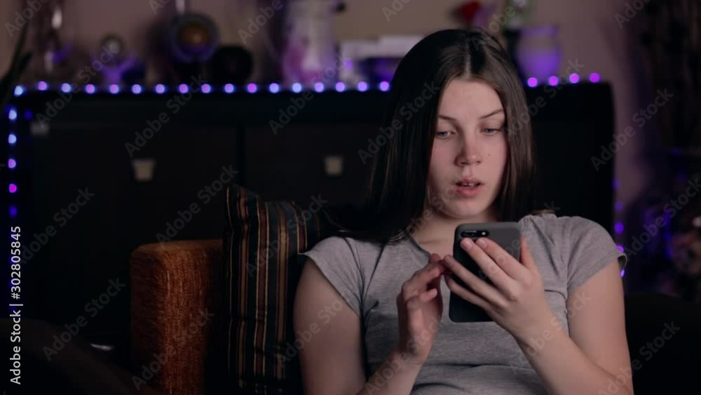 Shocked girl reading message via smartphone. Upset young woman holding cell phone at home. Bad news concept Shocked girl reading message via smartphone. Upset young woman holding cell phone at home. Bad news concept