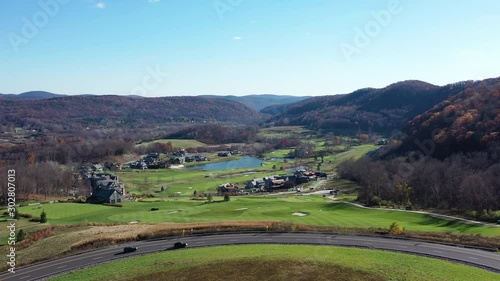 aerial view at Scenic Overlook, the drone camera hovers in place on a sunny day, views of the fall foliage on the mountains, a lake, golf course & treetops as two cars drive by below,  in Amenia, NY photo