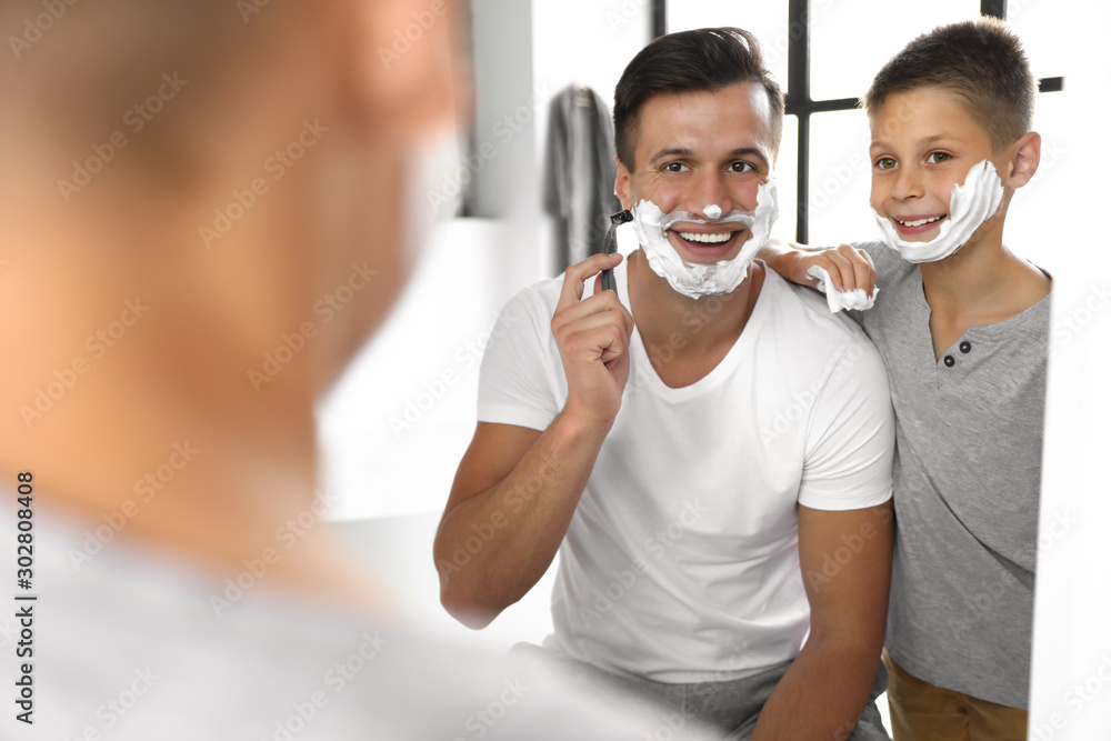 Dad showing his son how to shave near mirror in bathroom