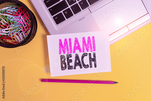 Conceptual hand writing showing Miami Beach. Concept meaning the coastal resort city in MiamiDade County of Florida Trendy laptop pencil squared paper container colored background photo