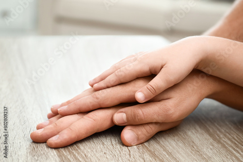 Happy family holding hands at wooden table indoors, closeup view