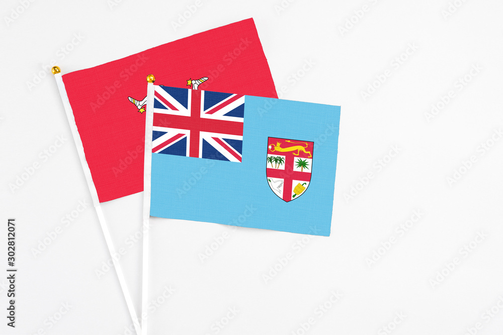 Fototapeta premium Fiji and Isle Of Man stick flags on white background. High quality fabric, miniature national flag. Peaceful global concept.White floor for copy space.