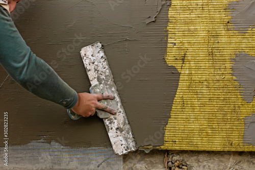 Plastrerer man plastering mineral wool slabs (rock wool, mineral cotton) insulation with reinforcing mesh and thermal glue mortar. Hand with spatula. Fiberglass insulation panels saving house heating